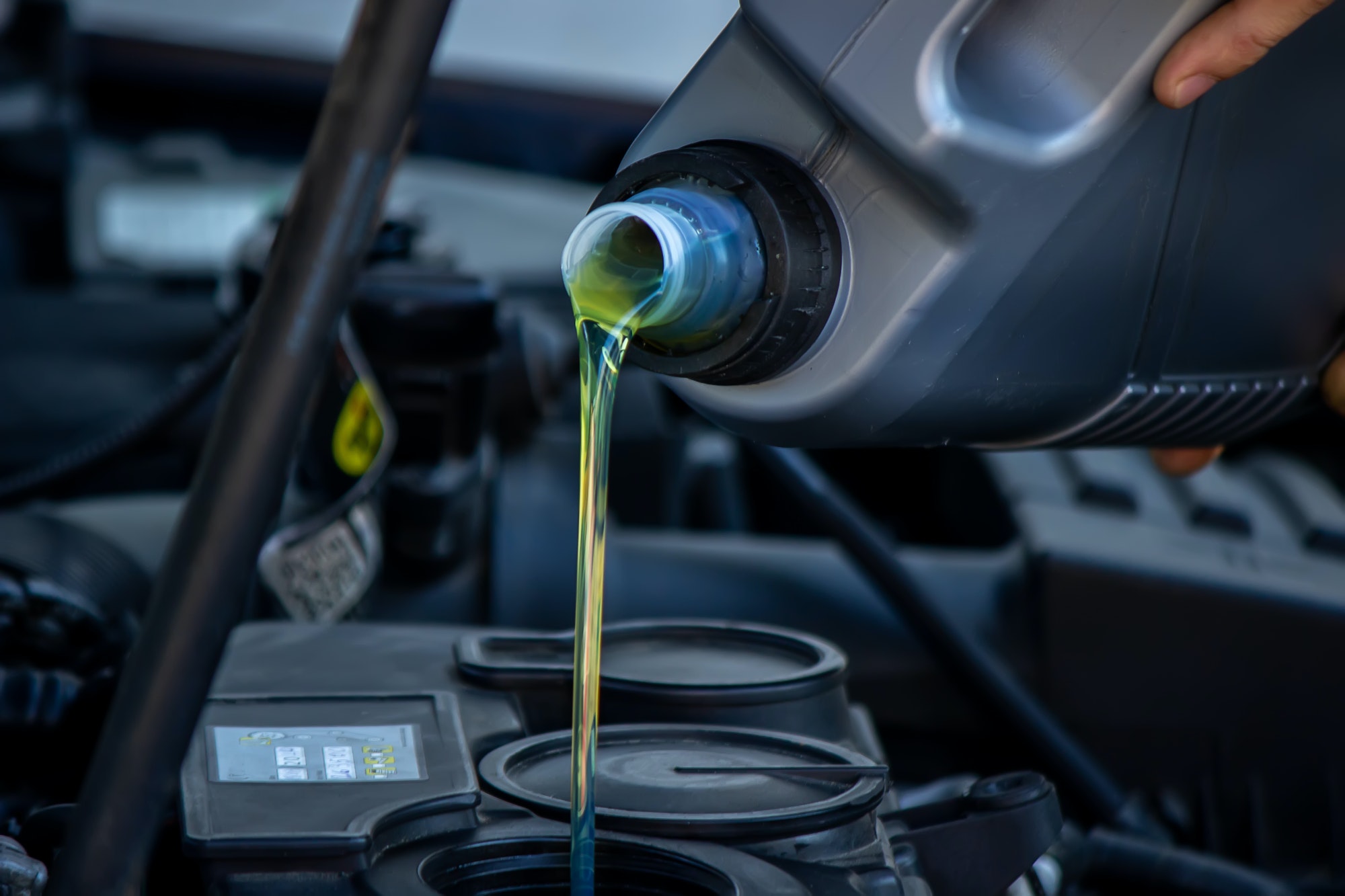 An auto mechanic changing oil pours oil into a car engine.