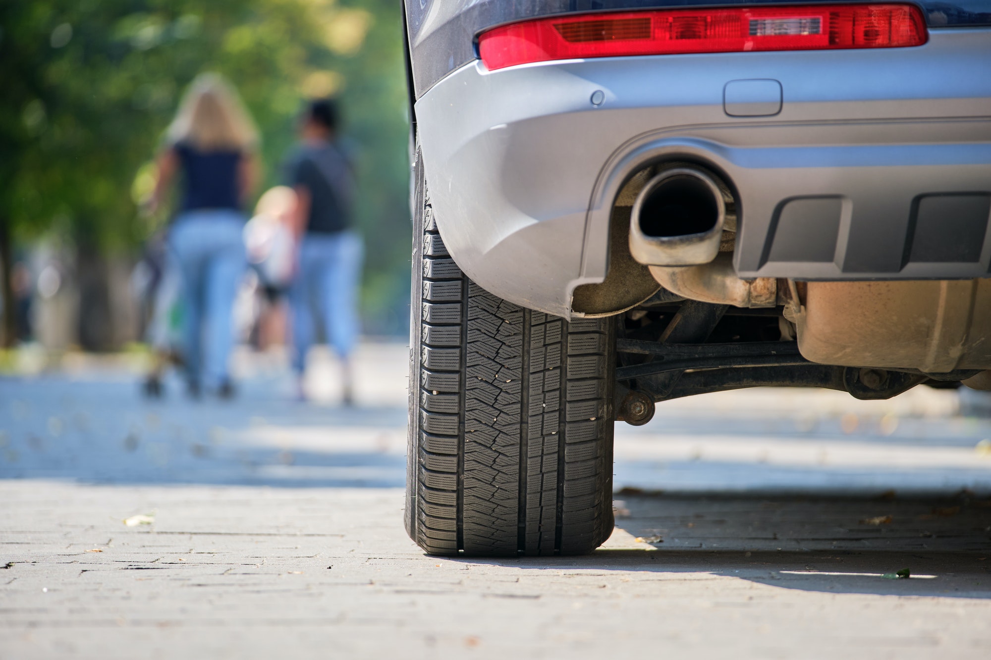 Close up of car rear wheel and exhaust pipe parked on city street side